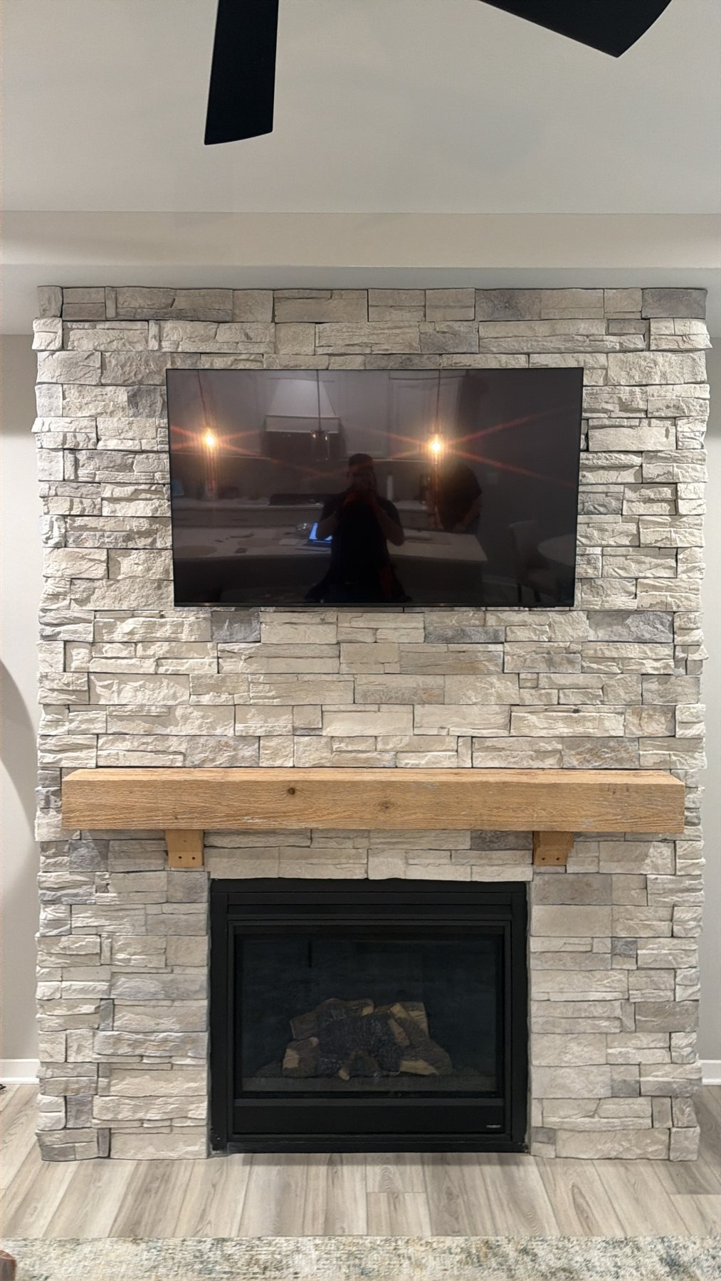TV Mounting on Stone-Faced Fireplaces Front view of TV above light stacked-stone fireplace and wood mantel